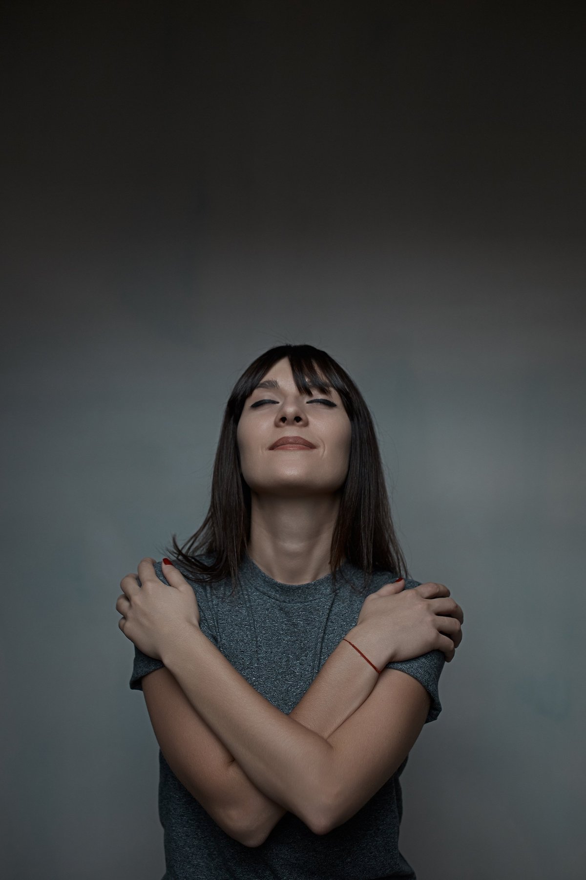 Close up portrait of young beautiful woman with dark hair embracing herself with closed eyes