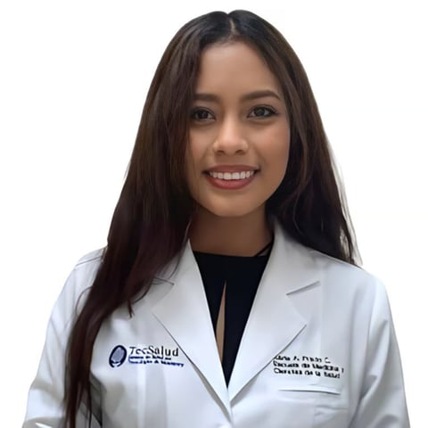 Professional headshot of a woman wearing a white medical coat with a logo, smiling at the camera against a white background